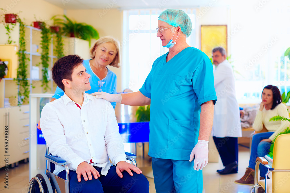Fototapeta premium surgeon and medical staff talking with young adult man in wheelchair, in hospital