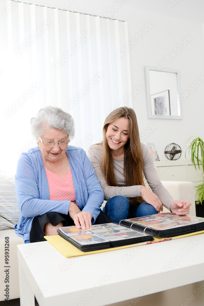 elderly woman with her young granddaughter at home looking at memory in family photo album elderly woman with her young granddaughter at home looking at memory in family photo album