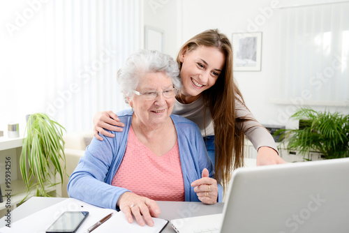 young woman helping an old senior woman doing paperwork and administrative procedures with laptop computer at home photo