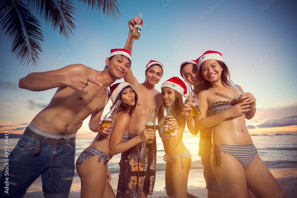 Young happy people on beach having Christmas party - obrazy, fototapety, plakaty 