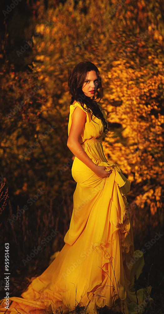 Young woman in the yellow dress with autumn leaves 