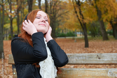 redhead girl listen music in city park, fall season