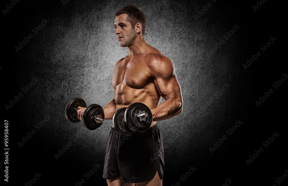 Bodybuilder doing shoulders exercises with dumbell over grey wal