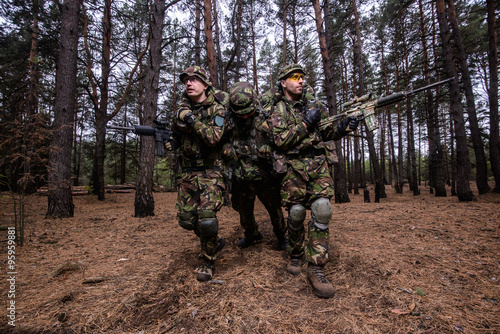 Evacuation of wounded soldier in forest/Two armed men in military uniform evacuate wounded soldier from the battlefield