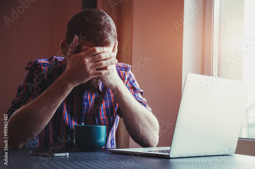 Foto Stressed man with head in hands near laptop