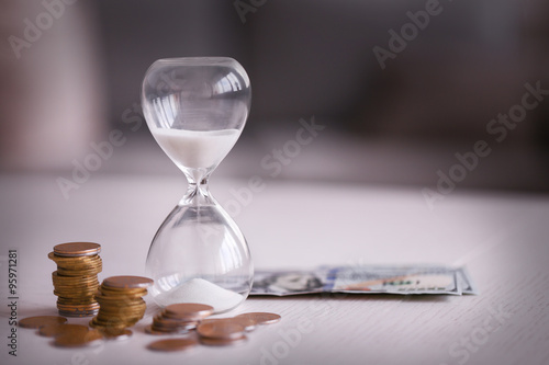 Hourglass with money on table on bright background