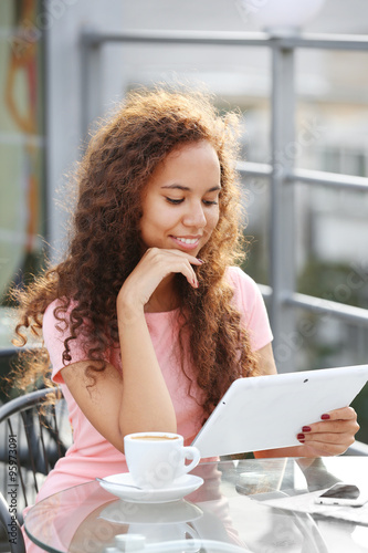 Beautiful young lady with tablet sitting at the summer terrace