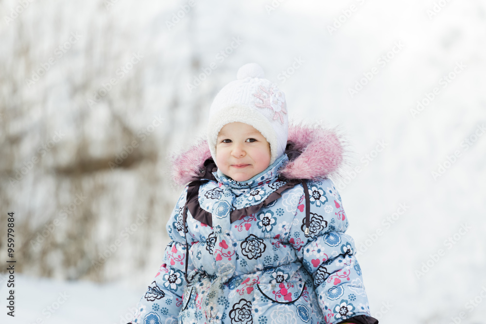 Head and shoulders portrait of toddler girl wearing white knitted hat and warm winter jacket