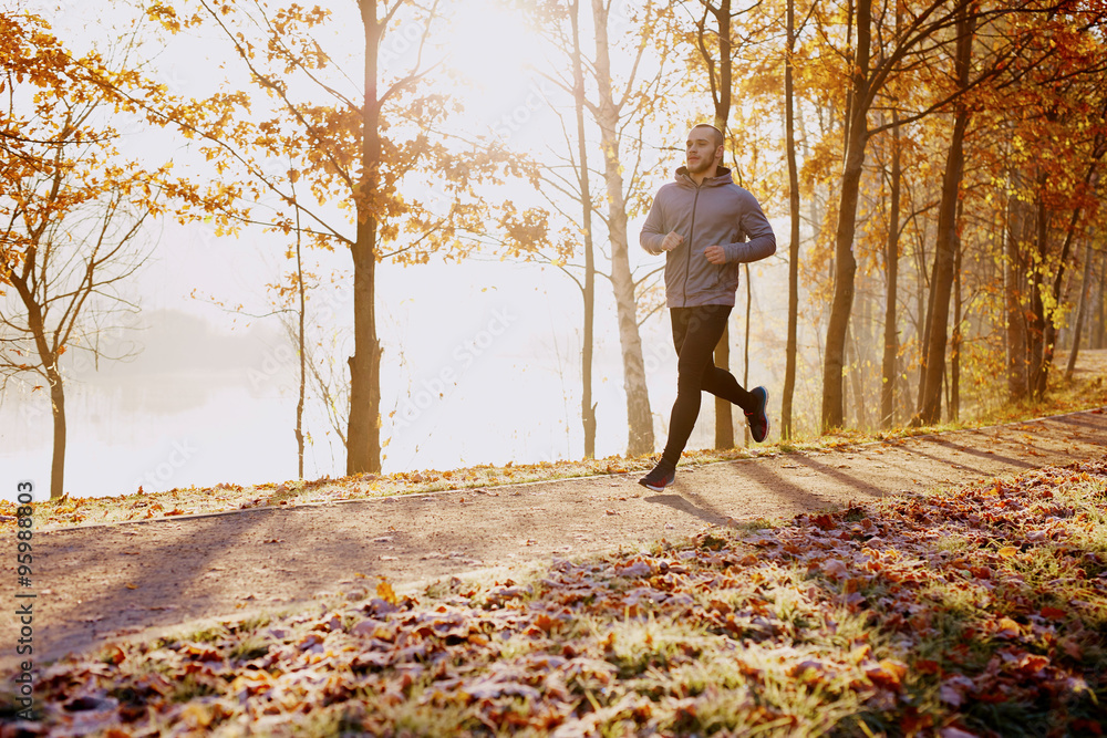Fit male runner training in the park during cold sunny autumn mo Fit male runner training in the park during cold sunny autumn mo