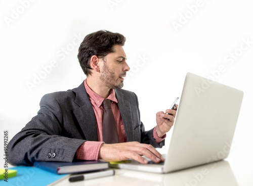 attractive businessman sitting at office desk working in stress on computer laptop talking on mobile phone overworked