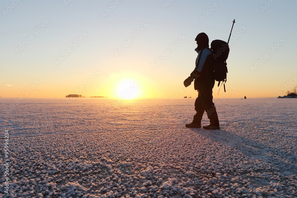 The man with a backpack going on ice on the river at sunset in the fall. River Ob, Russia