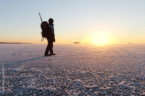 The man with a backpack going on ice on the river at sunsetin the fall. River Ob, Russia photo