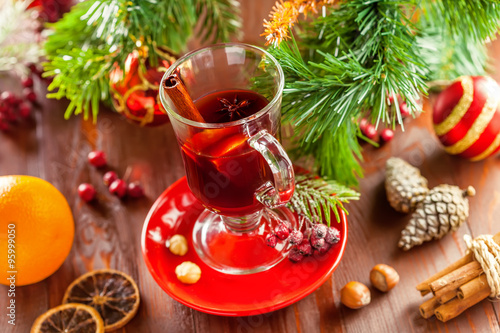 Glass of traditional hot drink on table by Christmas tree with decorations. Mulled wine.