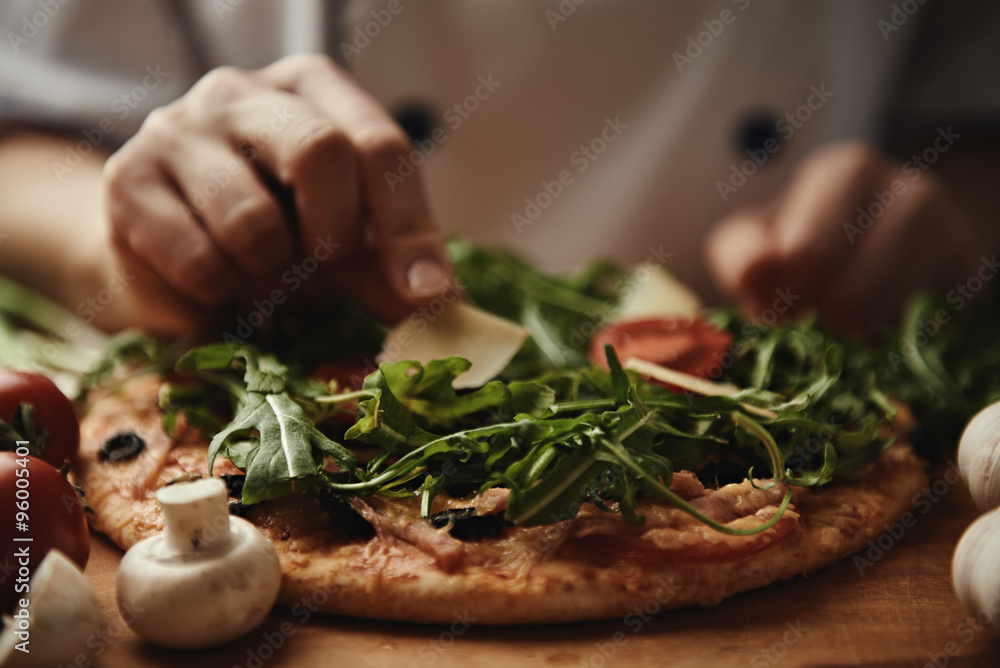 Female baker finishing pizza preparation by putting cheese slice on the top.  - obrazy, fototapety, plakaty 