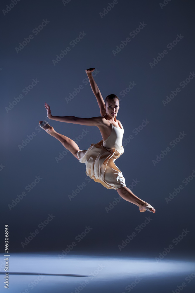 Young beautiful dancer in beige dress jumping on gray background Young beautiful dancer in beige dress jumping on gray background