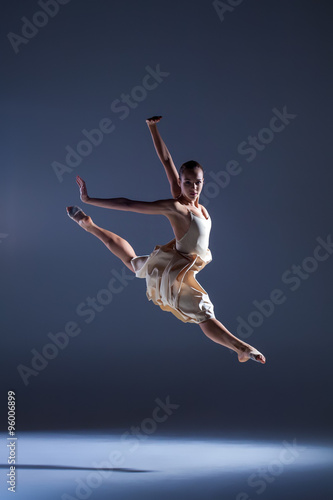 Young beautiful dancer in beige dress jumping on gray background