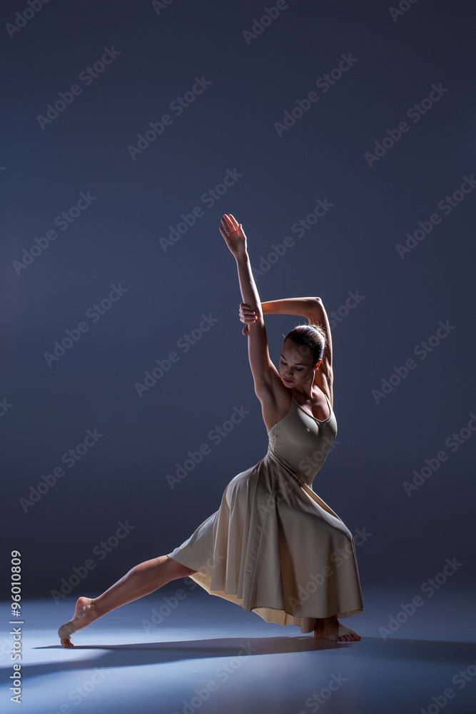 Fototapeta premium Young beautiful dancer in beige dress dancing on gray background