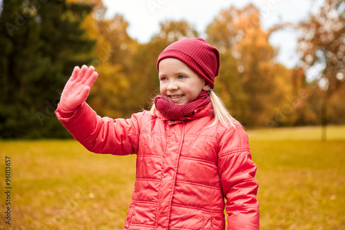 happy little girl waving hand in autumn park