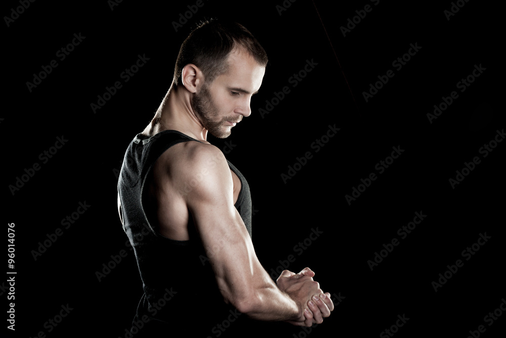 muscular man, clasps hands in fist, black background, place for text on the right muscular man, clasps hands in fist, black background, place for text on the right