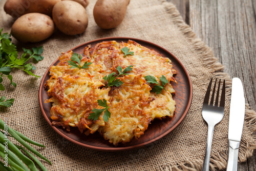 Homemade traditional potato pancakes or latke Hanukkah celebration food in rustic clay dish on vintage wooden background