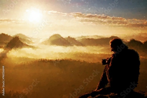 Watercolor paint. Paint effect. Photographer silhouette above a clouds sea, misty autumn mountains at daybreak.
