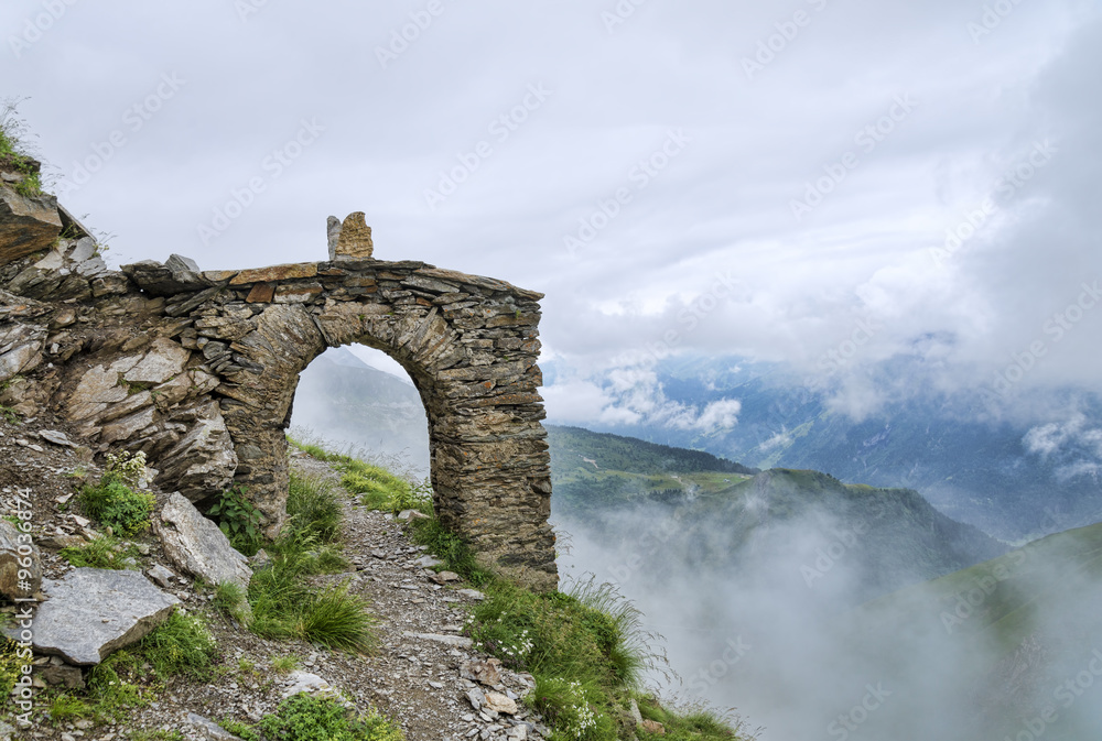 Arch fragment of ancient building among summer alpine landscape