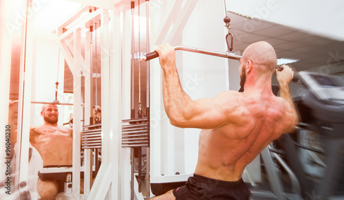 Man doing back pullups in the mirror at the gym with a energy powerful look and feel with soft filters applied suggesting a hard workout photo