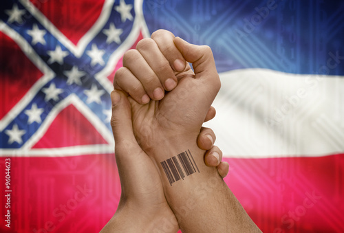 Barcode ID number on wrist of dark skinned person and USA states flags on background - Mississippi