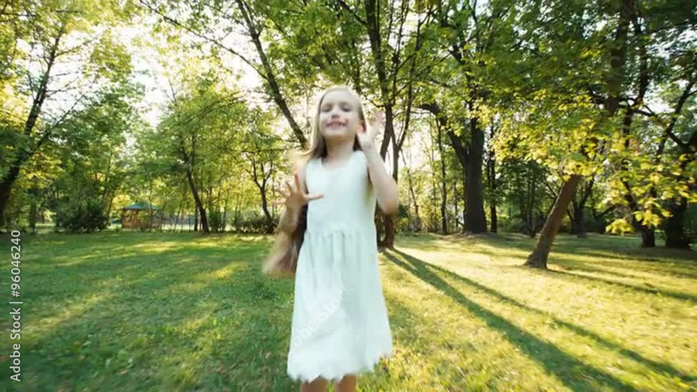 Girl running in the park at camera. Happy child in the white dress. Lens flare. Against the sun Girl running in the park at camera. Happy child in the white dress. Lens flare. Against the sun