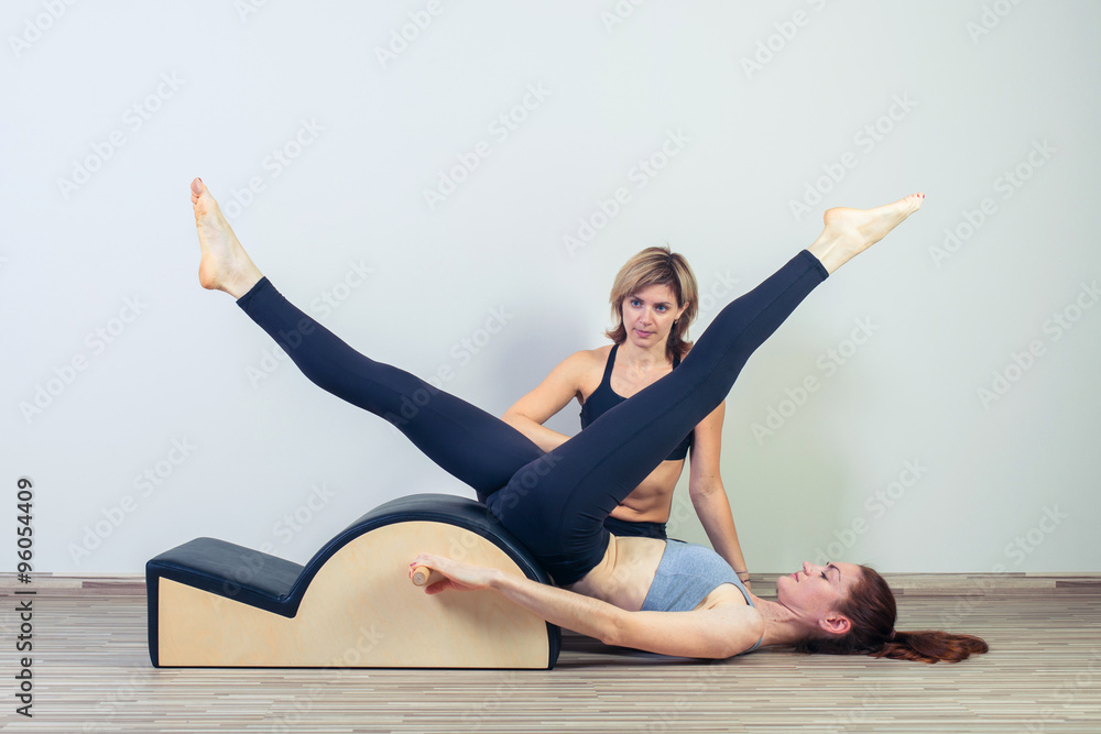 Pilates, fitness, sport, training and people concept -  woman with instructor doing  exercises on small barrel