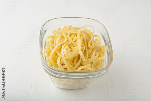 a small portion of linguini pasta in a glass storage container on white background