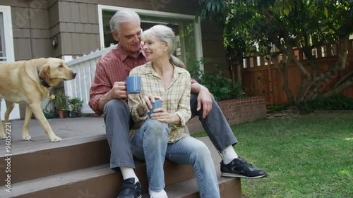 Senior couple having coffee petting dog in their yard