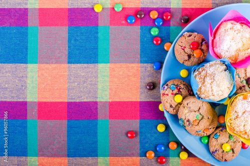 Fresh homemade muffins and cookies with color chocolate coated candies on a colorful checkered kitchen towel. Free space for your text