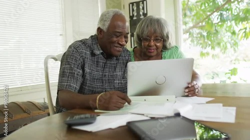 Happy senior African couple paying off bills on laptop