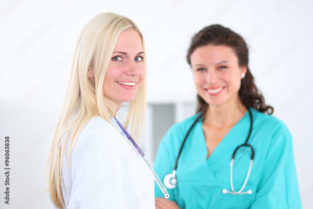 Beautiful young smiling female doctor standing at hospital with doctor on the background. Medical concept. Beautiful young smiling female doctor standing at hospital with doctor on the background. Medical concept.