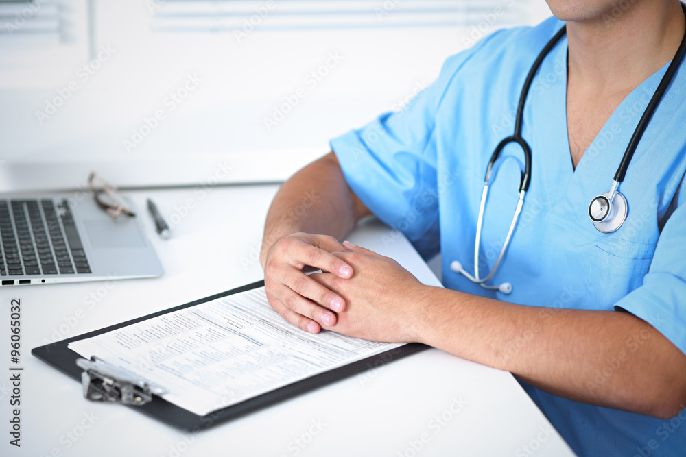 Portrait of unknown male surgeon doctor sitting at the table in hospital office, stethoscope Portrait of unknown male surgeon doctor sitting at the table in hospital office, stethoscope