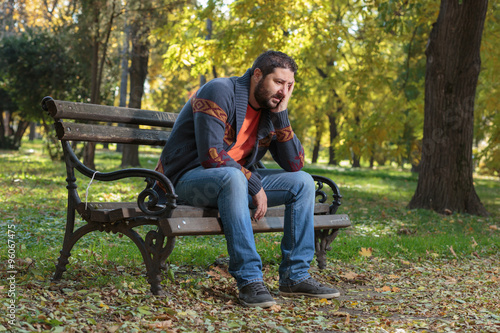 Shot of a grief-stricken man sitting on a park bench with his head in his hands