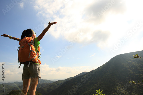 cheering young woman hiker open arms at mountain peak