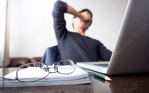man with his hand holding his face taking a brake from working with laptop computer and notebook with eye glasses on wooden desk. concept of stress/rest/tension/failed/discourage photo