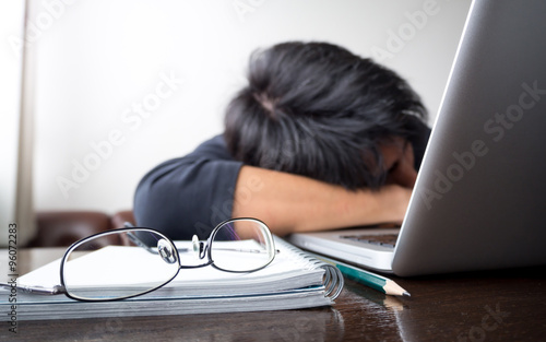 freelancer falling his face down taking a nap on wooden desk with laptop computer and notebook with eye glasses. concept of tired/lazy