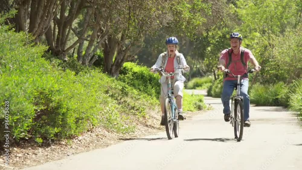Senior couple happily riding bikes outdoors on trail Senior couple happily riding bikes outdoors on trail