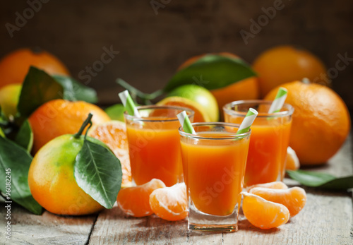 Fresh juice of ripe mandarins in a small glass with striped stra