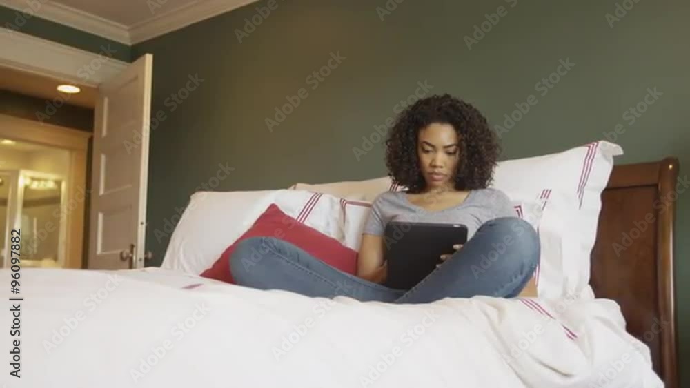 African woman sitting on bed using tablet at home African woman sitting on bed using tablet at home