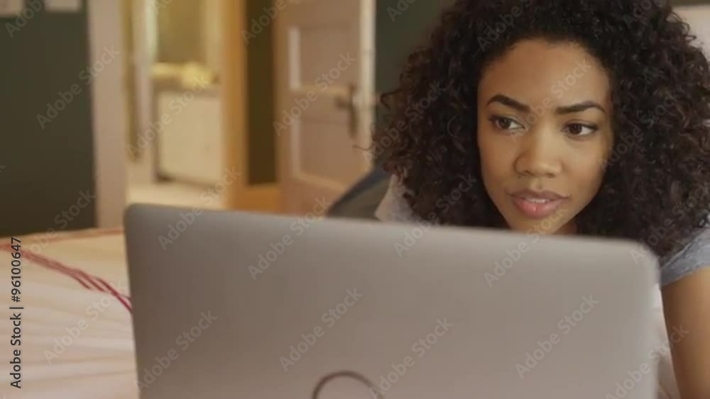 Happy African woman using laptop on bed