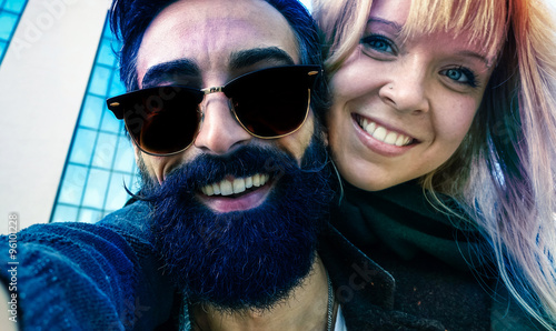 Bearded man and girlfriend taking selfie playing piggyback - Hipsters couple having fun with mobile phone - Two friends smiling for selfi photo outdoors - Modern concept of new urban fashion  trends