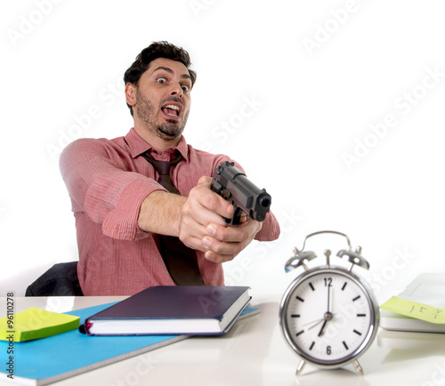 businessman in stress at office desk pointing hand gun to alarm clock in out of time and project deadline expiring