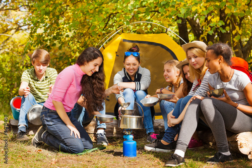 Teenagers cook soup in metallic pot near tent © Sergey Novikov