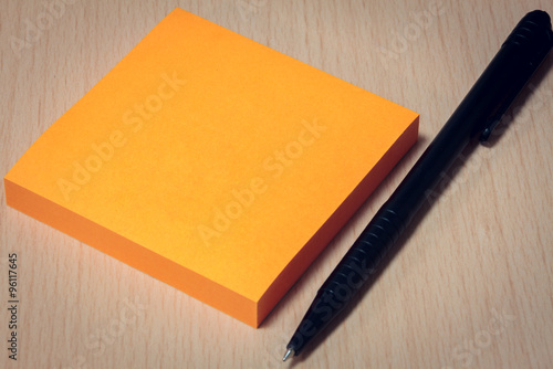 black pen orange paper on wood table background.