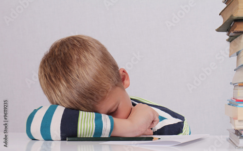 Cute tired school boy sleeping while doing homework