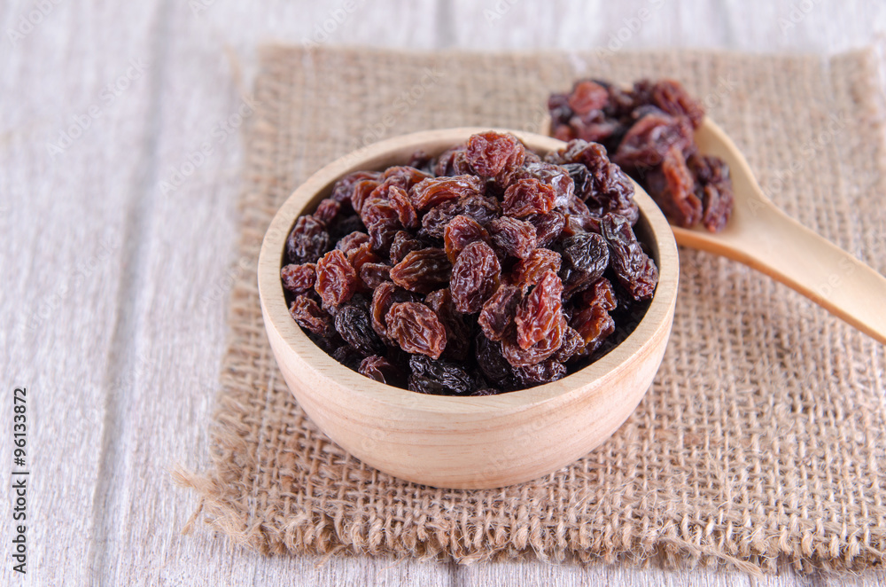 dry raisins in wooden bowl and spoon on white wooden table dry raisins in wooden bowl and spoon on white wooden table